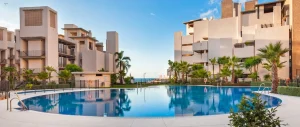 Luxurious beachfront property with a large swimming pool surrounded by modern buildings and palm trees, suggesting an upscale lifestyle offered by Rainbow Realty.