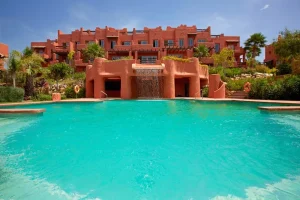 Modern apartment complex in Manilva, Spain, featuring a large swimming pool, available for rent through Rainbow Realty.